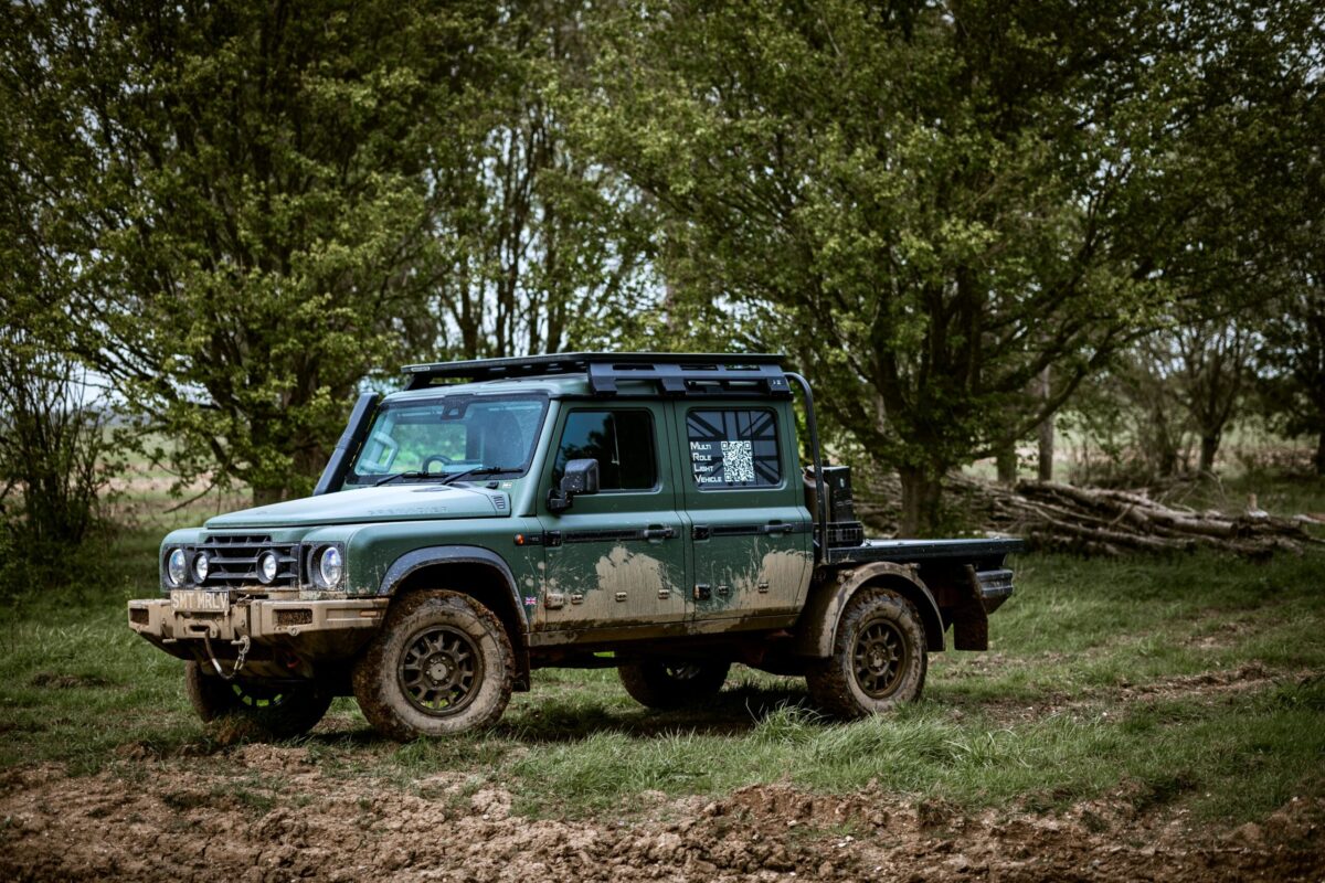 Green mud-splattered off-road SUV parked in a grassy field with dense trees in the background